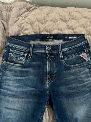  Replay jeans  - Snygga blå slim fit jeans från Replay med klassisk femficksdesign och diskreta slitningar. Jeansen har en liten logotypdetalj på fickan och kontrastsömmar. Perfekta för dig som gillar en modern och stilren look.
