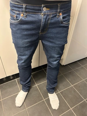 Levi's 511 mörkblå jeans - Storlek 164 Snygga mörkblå Levi's 511 jeans med klassisk femficksdesign och raka ben. Jeansen har den ikoniska röda Levi's-lappen på bakfickan och är tillverkade i mjukt bomullsjeansmaterial. Perfekta för en avslappnad och stilren look.