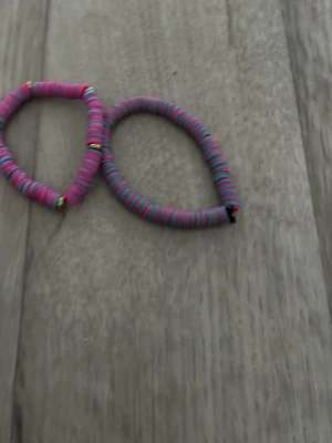 Färgglada armband med pärlor - Två elastiska armband med platta pärlor i rosa, blått och svart samt ett armband med rosa och vita pärlor. Alla har små guldfärgade detaljer mellan pärlorna. Perfekta för att addera färg till din stil.