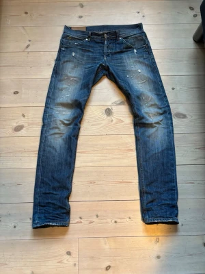Blå slitna jeans från dondup - Säljer ett par blå jeans från dondup med slitningar och raka ben. Jeansen har klassisk femficksdesign, låg midja och detaljerade slitningar framtill för en cool, avslappnad look. Perfekta för dig som vill mogga alla. Lite osäker på storlek men fråga på! Pris kan diskuteras 