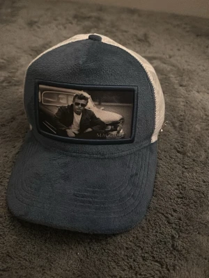 Riktigt fet maggiore kepa - Snygg truckerkeps från Maggiore i blått och vitt med mesh baktill. Framsidan har en svartvit patch med motiv av en person framför en bil. Kepsen har böjd skärm och justerbar passform. Perfekt för en cool och avslappnad stil.
