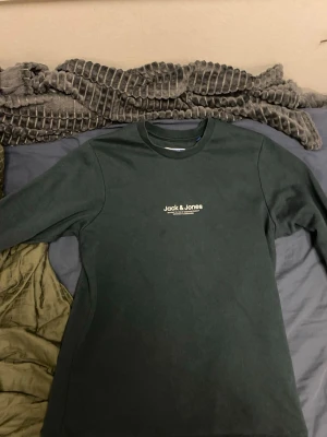 Mörkgrön sweatshirt från Jack & Jones - Mörkgrön sweatshirt från Jack & Jones med vit märke på bröstet med texten Jack & Jones. Varan är i mycket bra skick och knappt använd. Jag säljer den för att jag behöver pengar och vill bli av med gammla kläder. Jag köpte tröjan för 300kr skriv gärna om du är intresserad 