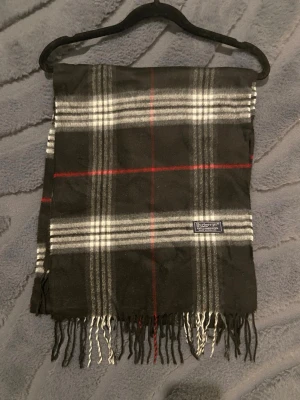 Klassisk Burberry Halsduk - Burberry halsduk 🤎  Klassisk Burberry-halsduk i det välkända svarta mönstret. En tidlös favorit som aldrig går ur stil.  ✨ Detaljer: – Material: lammull – Färg: Röd/Svart/Vit – Mått: 175 cm x 35 cm – Skick: Mycketbra – Original: ja  Perfekt till höst & vinter och funkar både casual och uppklätt. Skickas snabbt 📦  Pris kan diskuteras.