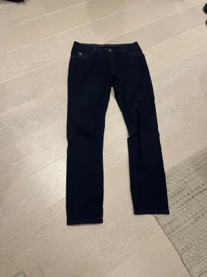 Mörkblå jeans från Hansen & Jacob - Snygga mörkblå jeans från Hansen & Jacob med raka ben och klassisk femficksmodell. Jeansen har diskreta röda detaljer vid sömmarna och en metallogo på fickan. Perfekta för dig som gillar stilrena och tidlösa plagg.