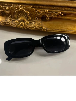 Svarta rektangulära solglasögon - Snygga svarta solglasögon med rektangulära bågar och glansig finish. Perfekta för en trendig look och passar till de flesta outfits. Klassisk design som ger en cool vibe.
