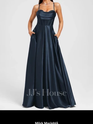 Mörk marinblå långklänning JJ's House - Elegant långklänning i mörk marinblå satin från JJ's House i stl 38. Klänningen har smala axelband, snörning i ryggen. Säljer pågrund av att jag bestämde mig för en annan färg men glömde gö retur på denna. Den är rättvis i storlek men går även att reglera med snörningen. Endast testad än gång och ser ut precis som på bilden(nyskick)! Nypris är 1577kr! 
