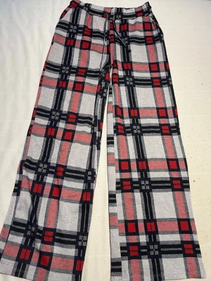 Rutiga mjukisbyxor i rött och svart - Mysiga mjukisbyxor med rutigt mönster i rött, svart och grått. Byxorna har resår i midjan med dragsko för skön passform och raka ben. Perfekta för chillkvällar hemma eller när du vill vara extra bekväm. Lite långa på mig som är 164cm.