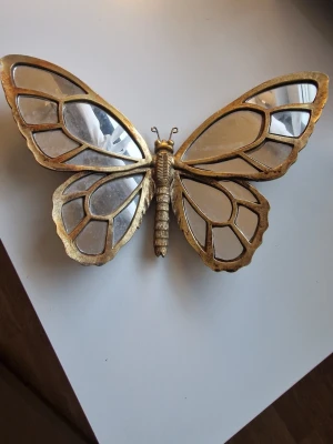 Guld färgad fjärill formad spegel - Snygg väggdekoration formad som en fjäril med guldfärgad ram och spegelglas i vingarna. Perfekt som unik inredningsdetalj för att ge rummet lite extra bling och personlighet.