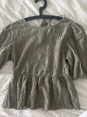 Grön topp - Mörk grön ton med öppen rygg och rosett, ballong armar. Aldrig använd men prislapp ej kvar.