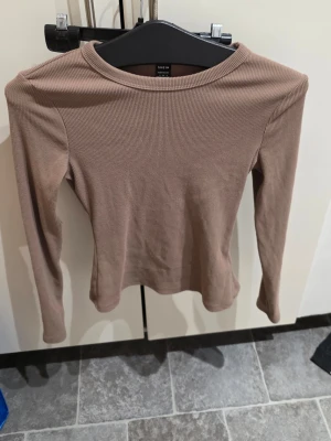 Beige ribbad långärmad topp SHEIN - Säljer en beige ribbad långärmad topp från SHEIN i storlek S. Toppen har en enkel, rund halsringning och är figurnära i modellen. Perfekt att styla med jeans eller kjol för en clean look.