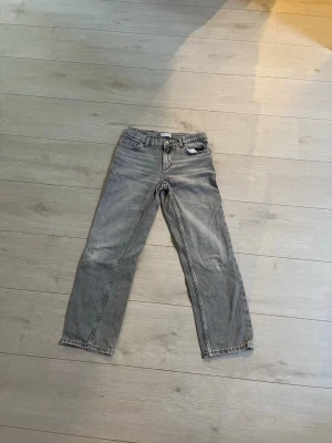 Grå raka jeans från Zara - Säljer ett par grå raka jeans från Zara med klassisk femficksdesign och knappgylf. Jeansen har en avslappnad passform och är tillverkade i ett mjukt denimtyg. Perfekta för en casual och trendig look.