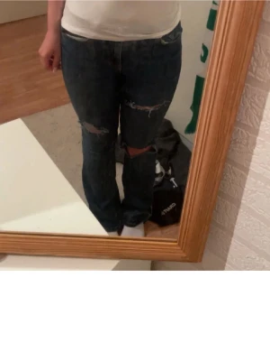 Mörkblå slitna jeans med hål - Säljer ett par mörkblå jeans som är bootcut och slitningar samt hål över knäna och normal hög midja. De passar perfekt för dig som är runt 160 då dem är i ginas petite modell. Aldrig använda!❤️