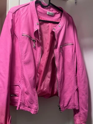 Rosa skinnjacka från repeat  - Snygg rosa skinnjacka från rapeat med silverfärgade dragkedjor och detaljer. Jackan har flera fickor med dragkedja och en klassisk bikerkrage med tryckknapp. På lappen står det XXL men den är inte oversized så passar endast för S/M