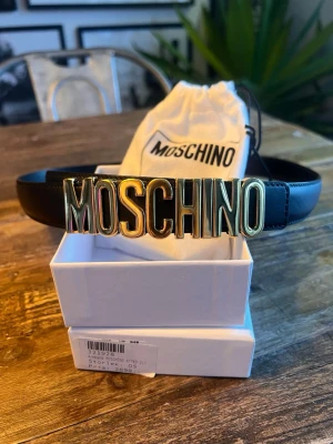 Moschino bälte  - Moschino Couture skärp – nyskick  Snyggt och stilrent Moschino Couture-skärp i svart läder med ikoniskt guldfärgat Moschino-spänne. Skärpet är i nyskick och knappt använt.  • Längd: 80 cm • Färg: Svart med guldfärgat spänne • Levereras med originalkartong och dustbag  Ett tidlöst statement-skärp som passar både vardag och fest.
