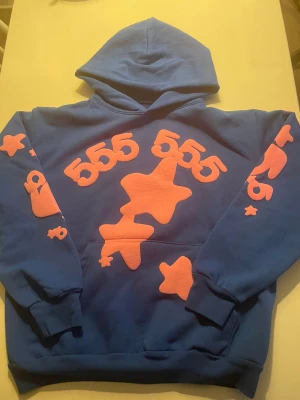 555 blå hoodie med rosa stjärnor XL - Säljer en blå hoodie från 555 i storlek XL med stora rosa stjärnor och siffror tryckta på bröstet och ärmarna. Tröjan har huva och magficka, samt ribbade muddar vid ärmslut och nederkant. Materialet är mjuk bomull, perfekt för chill dagar.