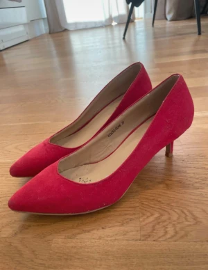 Röda pumps med spetsig tå från NLY Shoes - Snygga röda pumps från NLY Shoes med spetsig tå och låg klack. Skorna är gjorda i mocka-liknande syntetmaterial och har en klassisk, elegant form. Perfekt för dig som vill sticka ut med färg och stil. Storlek 37.
