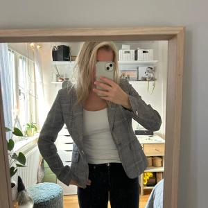 Grå rutig kavaj från HOPE - Snygg grå kavaj från HOPE med  rutig mönster och en knapp framtill. Modellen har figurnära passform, långa ärmar och två fickor fram. 