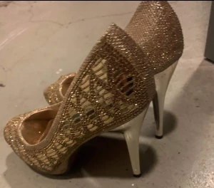 Glittriga guldiga pumps med öppen tå - Säljer ett par riktigt snygga pumps från Chic Aim i glittrigt guld med öppen tå och hög klack. Skorna har ett glittrigt mönster och mesh-detaljer som ger en extra lyxig känsla. Perfekta för dig som vill sticka ut och glänsa lite extra.passar st /39