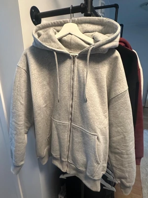 Helt ny Gizmo Hoodie Medium - Snygg grå hoodie från Gizmo med stor svart logga på ryggen. Tröjan har huva med snörning, två fickor fram och hel dragkedja. Tillverkad i 100% bomull för skön och mjuk känsla. Perfekt för chill dagar och streetwear-stil.