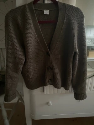 Brun stickad kofta från Lindex - Mysig brun stickad kofta från Lindex med v-ringad hals och stora knappar framtill. Koftan har långärmade ärmar och en loose passform som ger en chill vibe. Perfekt att slänga på sig när det är lite kyligt ute.