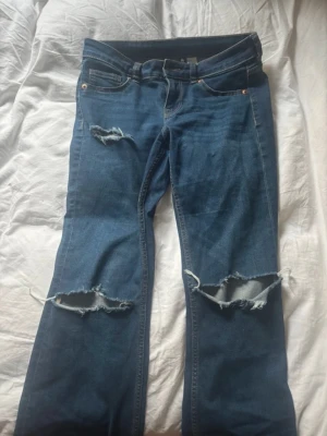 Blå bootcut jeans med slitningar från H&M - Säljer ett par blå jeans från H&M Divided i storlek 38.. Klassisk femficksdesign och low waist . Perfekt kondition