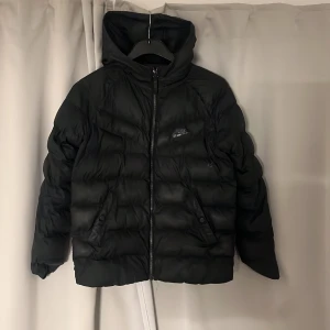 Svart pufferjacka från Nike - Svart pufferjacka från Nike med huva strl S/M