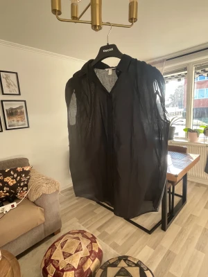 Svart transparent skjorta från H&M - Svart skjorta från H&M i transparent och lätt material, med coola fransdetaljer på axlarna och klassisk krage. Skjortan har en loose passform och är perfekt för dig som gillar att sticka ut med din stil. Snygg att bära lager på lager eller som den är.