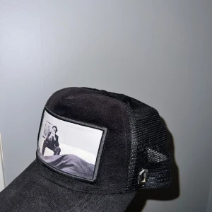 Svart OneCap keps med mesh och tryck - Säljer en svart keps från OneCap med mesh på sidorna och baksidan. Framtill finns ett stort svartvitt tryck med motiv av en person som sitter på en säng. Kepsen har justerbar storlek och cool streetstil.