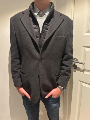 Mörkgrå rock från CP Collection - Snygg mörkgrå rock från CP Collection med klassisk passform och två framfickor. Kavajen har enkelknäppning och är tillverkad i ullblandning med slät finish. Perfekt för dig som vill ha en stilren look med lite edge.