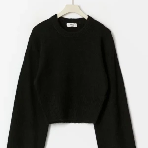 Svart croppad stickad tröja - Säljer en svart stickad tröja från Gina Tricot med rund hals och långa vida ärmar. Tröjan har en ribbad midja vilket gör den figurpassande. Använd endast 1 gång, jättebra skick, inte nopprig.