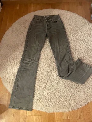 Gråa bootcut jeans - Gråa bootcut jeans med medel midja från Gina tricot. Säljer eftersom de är för små på mig som det syns på bilderna🥹Finns ett litet hjärta målat i bläck på ena knät🥲 kontakta mig för mer info💕