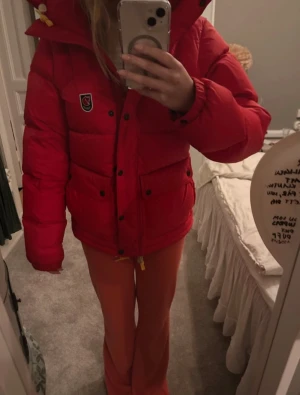 Fjällräven jacka  - Säljer en röd pufferjacka från Fjällräven med huva och gul snörning. Jackan har svarta knappar, dragkedja och klassisk Fjällräven-logga på bröstet. Perfekt för kalla dagar med sin tjocka och fluffiga design. Storlek s men sitter som xs ❤️ Passar dig som gillar färg och vill sticka ut. Osäker på modell då jag ej andvänd den på länge . Snörena är lite slitna ❤️ värdens varmaste jacka ❤️bild 2 är min ! 