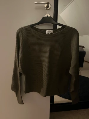 Ribbad grön långärmad tröja ONLY - Snygg ribbad tröja från ONLY i en mörkgrön färg. Modellen har rund hals och långa ärmar, perfekt för dig som gillar stilrena och enkla plagg. Materialet är mjukt och stretchigt, vilket gör den skön att bära. Passar dig som vill ha en basic tröja med lite struktur.