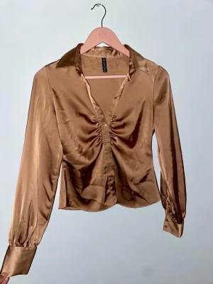 Guldaktig blus, New Yorker - Säljer denna eleganta & snygga blus i satintyg ifrån Newyorker då den inte passade mig. Behöver endast strykas & blir som ny! Kvittot finns inte kvar och blusen har hängt i garderoben endast.   Storlek S/36 🌸