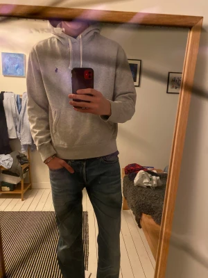 Ralph Lauren Hoodie  - Snygg ljusgrå hoodie från Ralph Lauren med klassisk broderad logga på bröstet. Tröjan har huva med vita snören, känguruficka och är tillverkad i mjuk bomullsmix. Perfekt för chill dagar och enkel att matcha med jeans eller joggers. Skriv om du har frågor! 