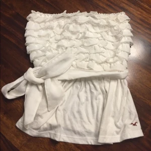 Vit bandeau tubtopp med volanger från Hollister - Supersöt vit bandeau tubtopp från Hollister med volanger upptill💖knytbandet saknas men går att sätta dit eget 