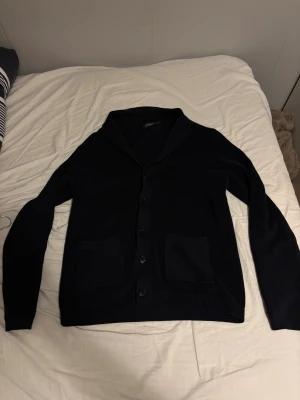 Mörkblå cardigan från Dressmann - Snygg mörkblå kofta från Dressmann i storlek M. Koftan är ribbstickad med långa ärmar, två små framfickor och knappar hela vägen.