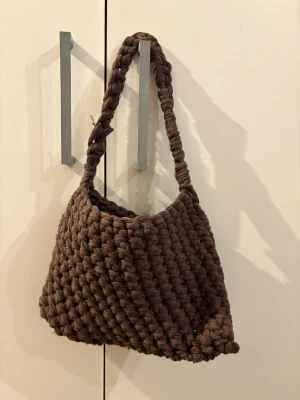 Brun virkad axelväska - Säljer en brun virkad axelväska. Väskan har en mjuk och chunky look, perfekt för dig som gillar handgjorda accessoarer. Materialet är mjukt och ger en cool, unik vibe till din outfit. Lite fransig i handtaget.