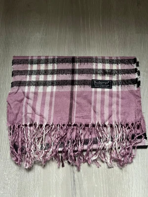 Rutig rosa halsduk från Burberry - Snygg rutig halsduk från Burberrys i en ljusrosa ton med inslag av vitt och svart. Gjord i 100% lammull. Stilren och inga skador. Perfekt julklapp till en bra peng! 
