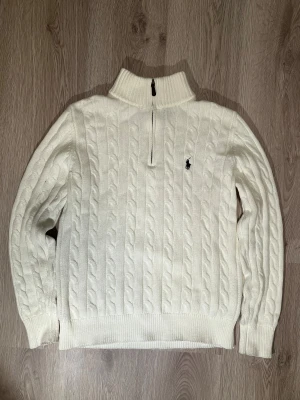 Vit stickad tröja Polo Ralph Lauren S - Har blivit använt 2-3 gånger och den är i toppskick. Säljer en vit stickad tröja från Polo Ralph Lauren i storlek S. Tröjan har kabelstickat mönster, half zip i halsen och broderad logga på bröstet. Ribbstickade muddar och krage ger en snygg och klassisk look. Perfekt för dig som gillar stilrena och tidlösa plagg. 