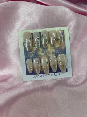 SilverGlam (S);Medium Almond - Säljer ett set handgjorda press-on naglar i nude med silverglitter och små holografiska stenar. Naglarna är i en medium mandelformade och har en lyxig vibe med skimrande detaljer. Perfekt för dig som vill ha snygga och trendiga naglar utan att gå till salong.S: 15 mm, 11,5 mm, 12 mm, 11 mm, 9 mm 