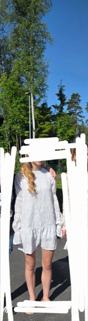 Vit kort klänning med volangärm - Superfin vit kort klänning med broderade blommor och volangdetaljer på ärmar och nederkant. Långa ärmar och rund halsringning ger en söt vibe. Perfekt för sommarens alla tillfällen!