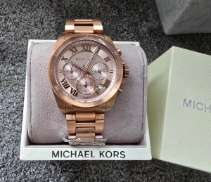 Roséguld klocka från Michael Kors - Stilren Michael Kors-klocka i roséguld med metallänk. Elegant urtavla med romerska siffror, kronograf och datumvisning. Klockan är helt ny och oanvänd med skyddsplast kvar och levereras i originalask med kudde och manual. Perfekt som present eller julklapp.