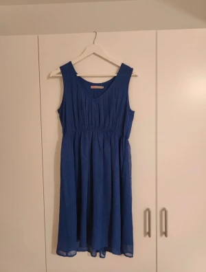 Glittrig mörkblå klänning  - Blä glittrig klänning från Saint Tropez med v-ringning och veckad överdel. Resår i midjan, luftig kjol.