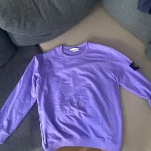 Lila sweatshirt från Stone Island, storlek S  - Säljer en lila sweatshirt från Stone Island med klassisk patch på ärmen. Tröjan har rund halsringning, långa ärmar och är gjord i mjuk bomull. Perfekt för dig som gillar streetwear och vill sticka ut med färg.