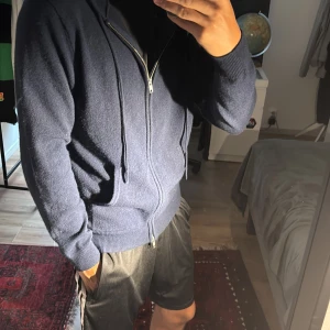 Mörkblå hoodie med dragkedja - Säljer en mörkblå hoodie med dragkedja och huva. Tröjan har långa ärmar, fickor framtill och en clean look utan mönster eller logga. Perfekt för chill dagar och enkel att matcha med jeans eller joggers. Materialet känns mjukt och bekvämt mot huden. Den är i nyskick! 100% Kashmir!