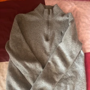 Grå stickad half zip-tröja Polo Ralph Lauren - Snygg grå stickad tröja från Polo Ralph Lauren med half zip och hög krage. Tröjan har lång ärm och diskret logga på bröstet. Perfekt för dig som gillar klassisk stil med en chill vibe. Passar till jeans eller chinos. Som sagt den var storlek L men blev mindre i tvätten. Och även så har den två hål som knap syns 