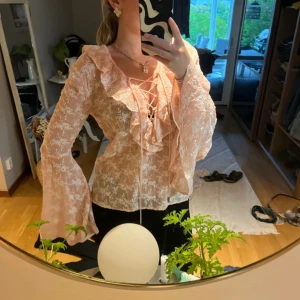 Rosa blus med broderade blommor och vida ärmar från Guess - Så fin!! Broderade blommor. Aprikos/rosa. Så fina vida ärmar. Knytning vid brösten. Storlek Xs men passar mig som är en S också. V ringad. Volanger vid brösten.