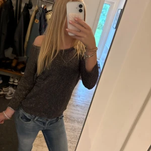 Glittrig offshoulder tröja från ONLY - Säljer en mörkgrå glittrig stickad tröja från ONLY i storlek S. Tröjan har offshoulder-design och trekvarts långa ärmar, perfekt för dig som vill ha något snyggt och bekvämt med lite extra bling. Superfin till jeans eller kjol!