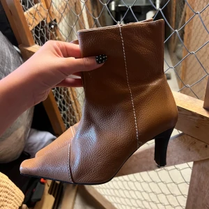 Bruna stövletter med klack och spetsig tå - Bruna stövletter i skinn med markerad vit söm och spetsig tå. Modellen har en smal hög klack. Storlek 39, men passar mig som har 37/38. Klacken kan behövas klackas om. Köpt begagnade för 499kr